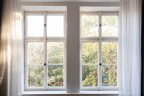 Two residential windows with white, transparent curtains on either side