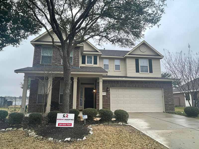 Front view of a mid-class home recently worked on by Robin's Roofing - their sign is on the front lawn