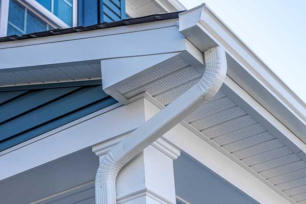 Close up of a white k-style gutter system and downspout, all attached to the fascia of a blue mid-class home
